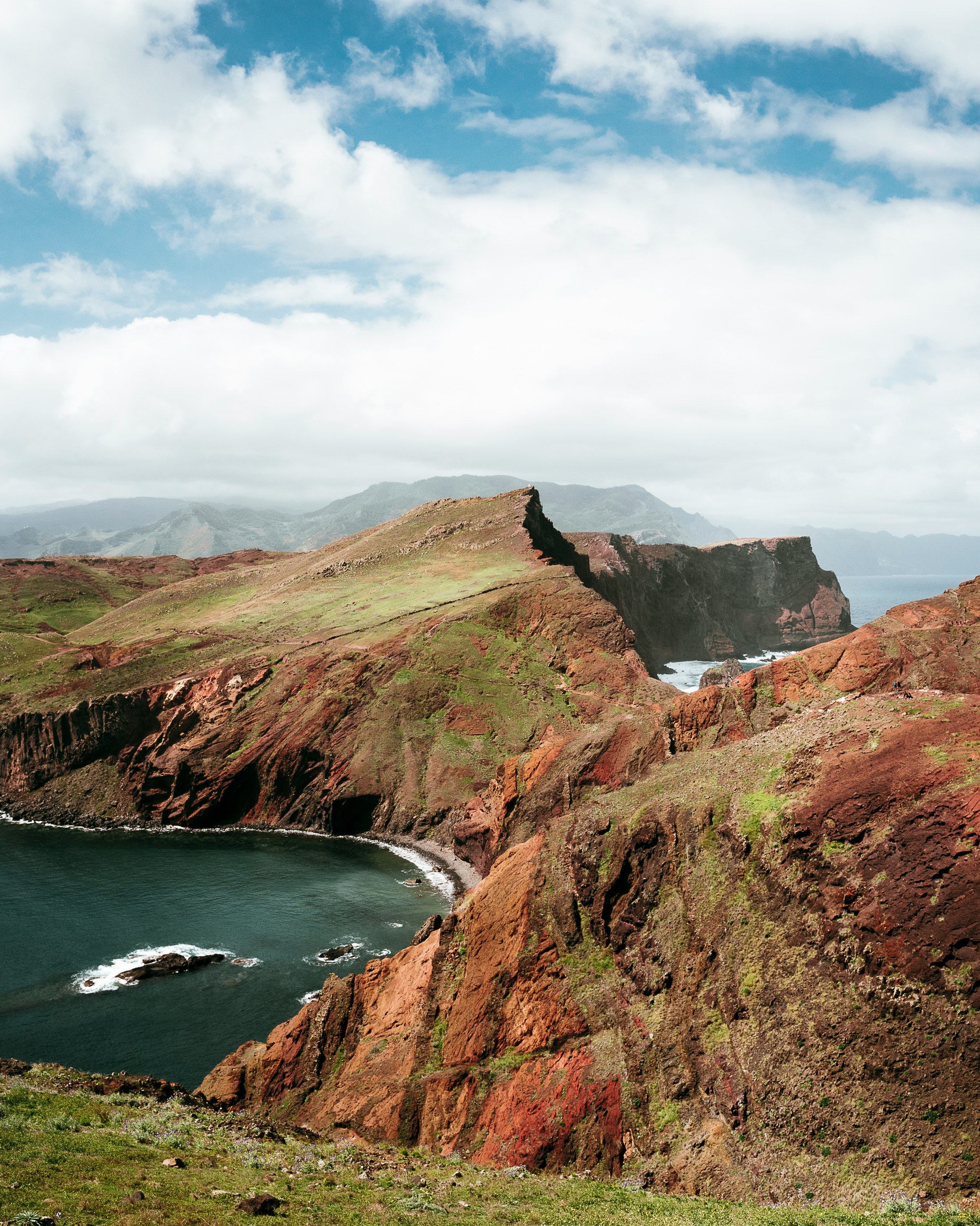 green and brown mountain beside body of water under white clouds and blue sky during daytime